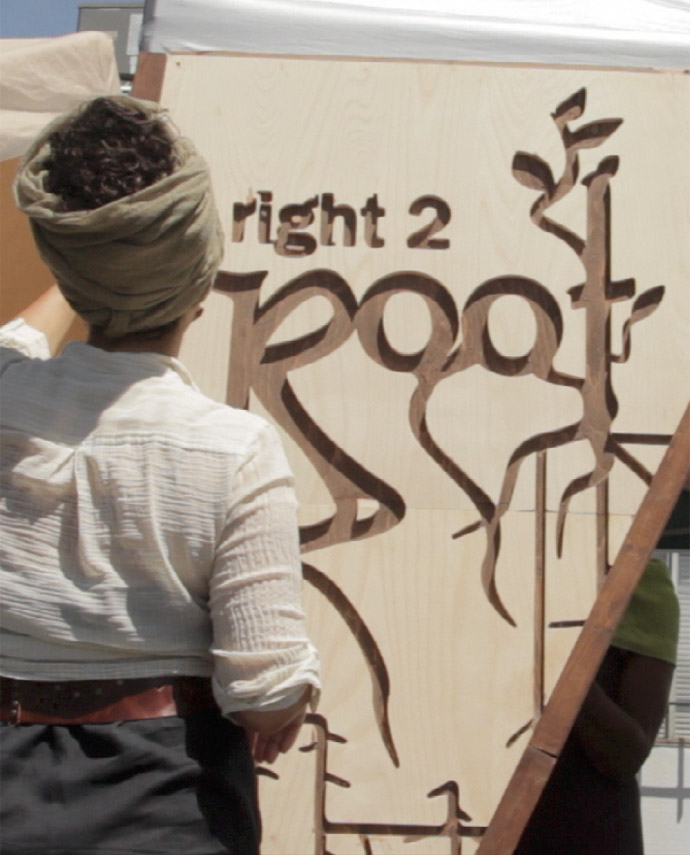 Woman with her back turned, standing in front of Right2Root wooden sign